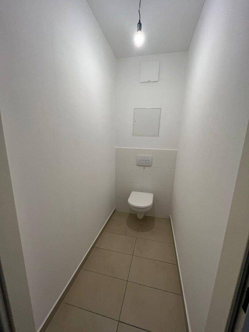 Kompaktes Gäste-WC mit wandhängender Toilette und hellen Fliesen an Boden und Wänden.