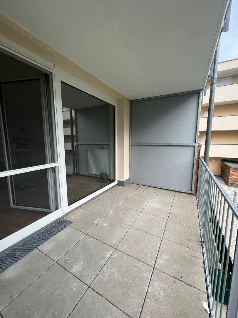 Heller Balkon mit Fliesenboden und Zugang zum Innenbereich, umgeben von einer Metallbrüstung.