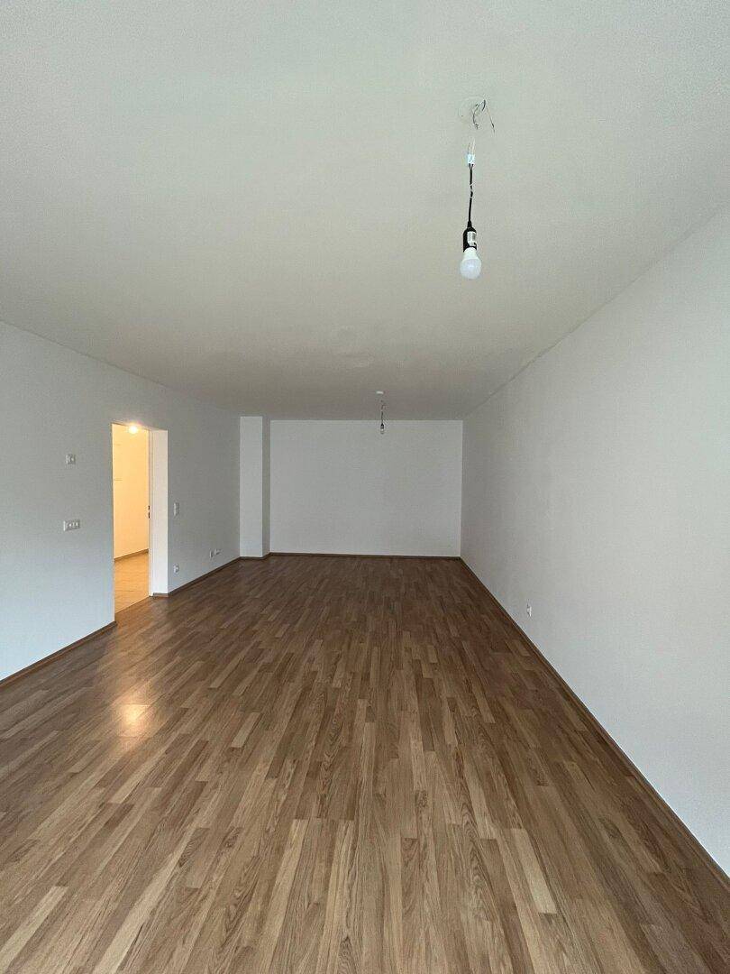 Geräumiges, leeres Wohnzimmer mit hellem Laminatboden und weißen Wänden, bereit zur Einrichtung.