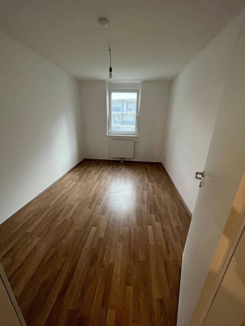 Helles Schlafzimmer mit Laminatboden, weiß gestrichenen Wänden und einem Fenster für Tageslicht.