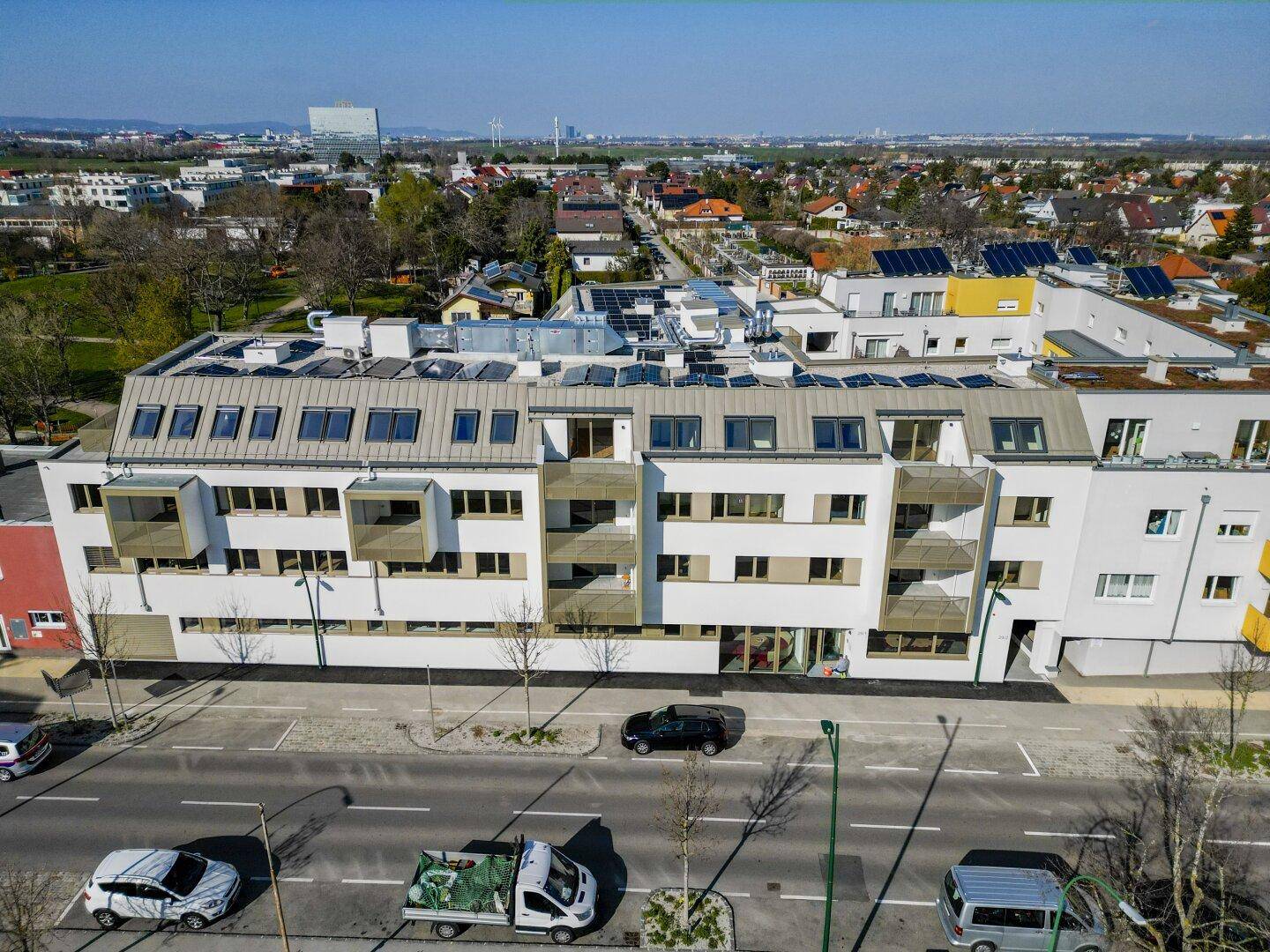 Luftaufnahme eines modernen Wohngebäudes mit weißer Fassade, Solarpaneelen und Blick auf die Umgebung.
