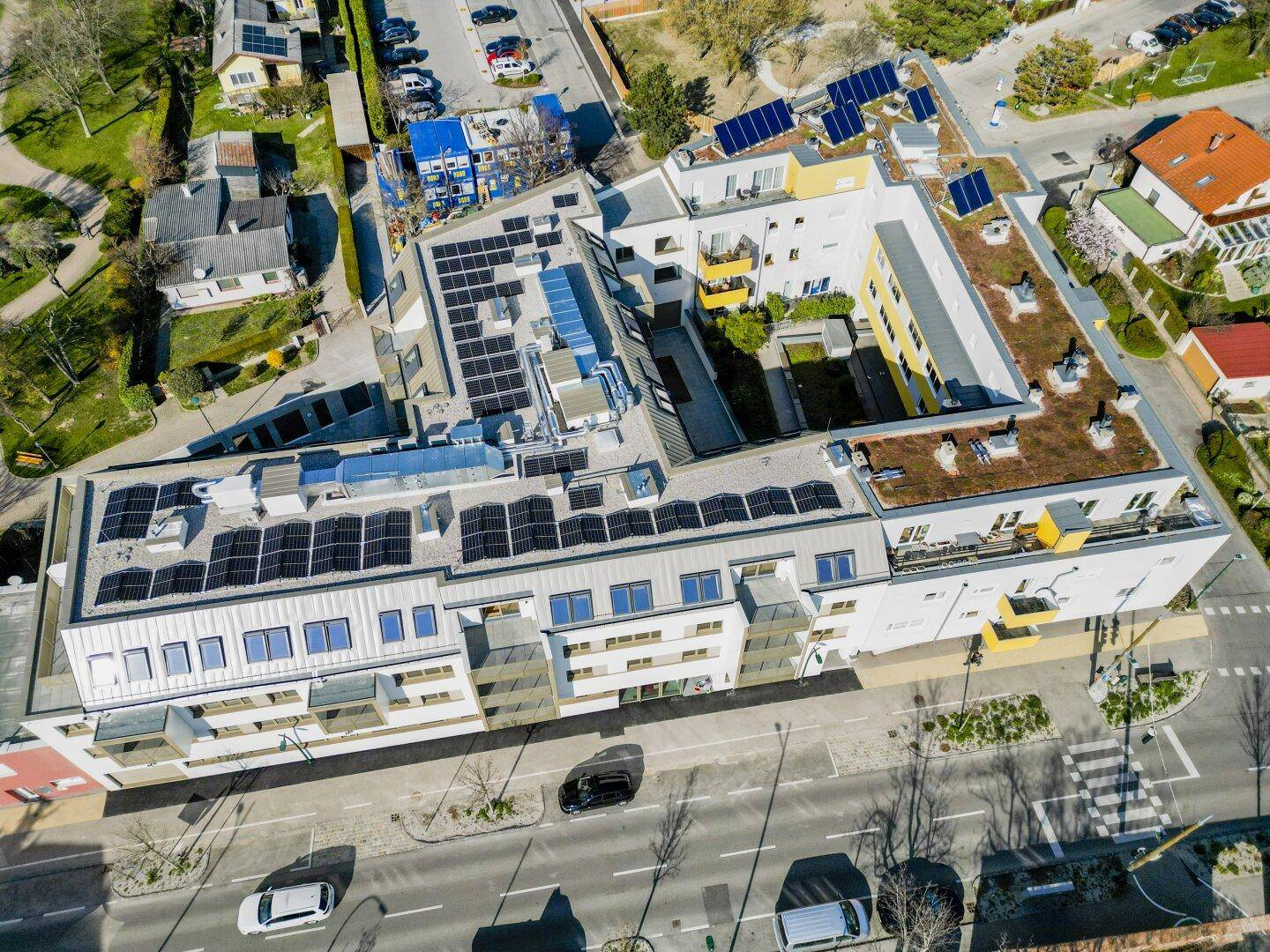 Weitläufige Luftaufnahme eines Wohnkomplexes mit zahlreichen Solarpaneelen und begrünten Dächern.