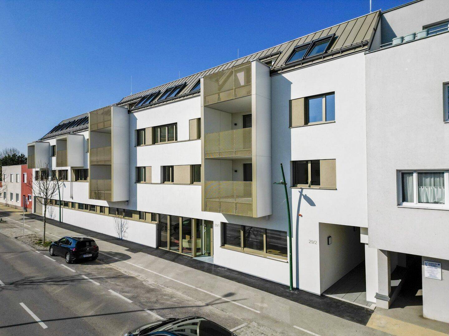 Moderne weiße Fassade eines Wohngebäudes mit Balkonen und großen Fenstern an einer Straße.