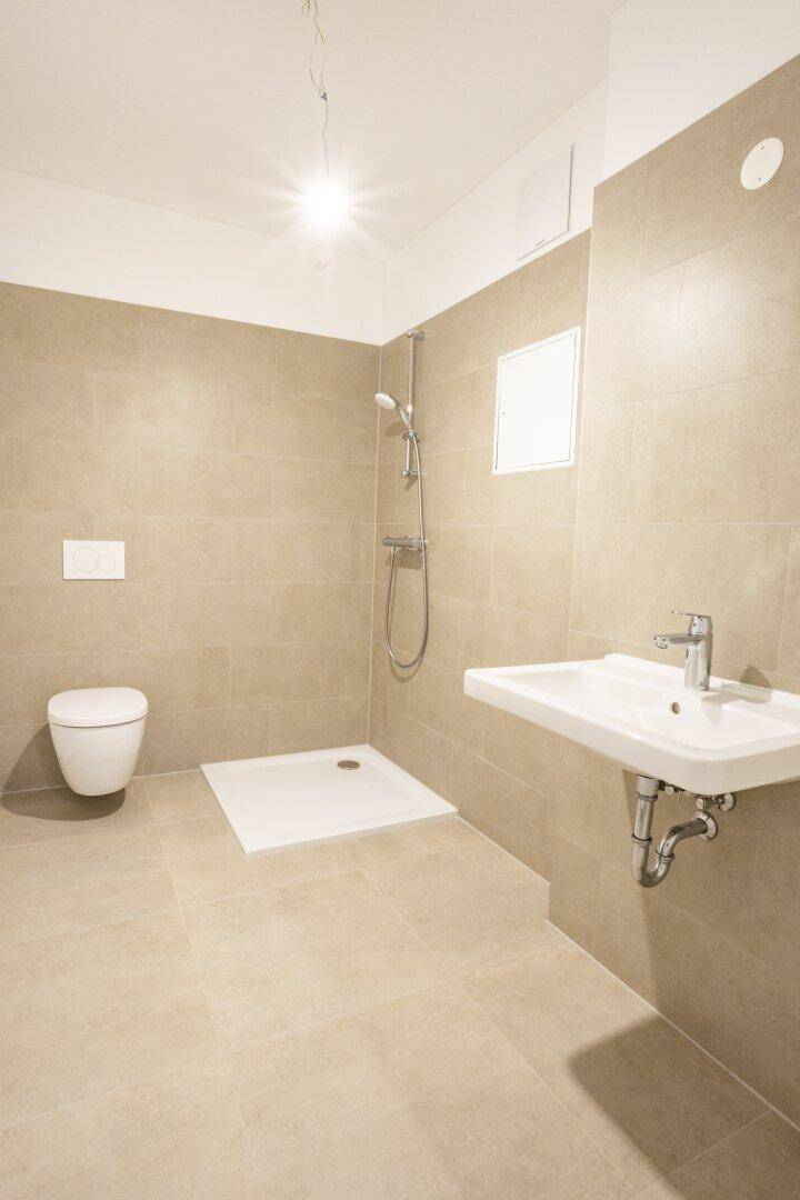 Modernes Badezimmer mit beigefarbenen Fliesen, Dusche und wandhängendem WC.