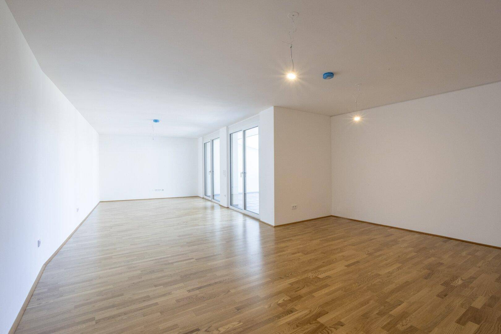 Heller Wohnbereich mit Parkettboden und großen Fenstern, die viel Tageslicht hereinlassen.