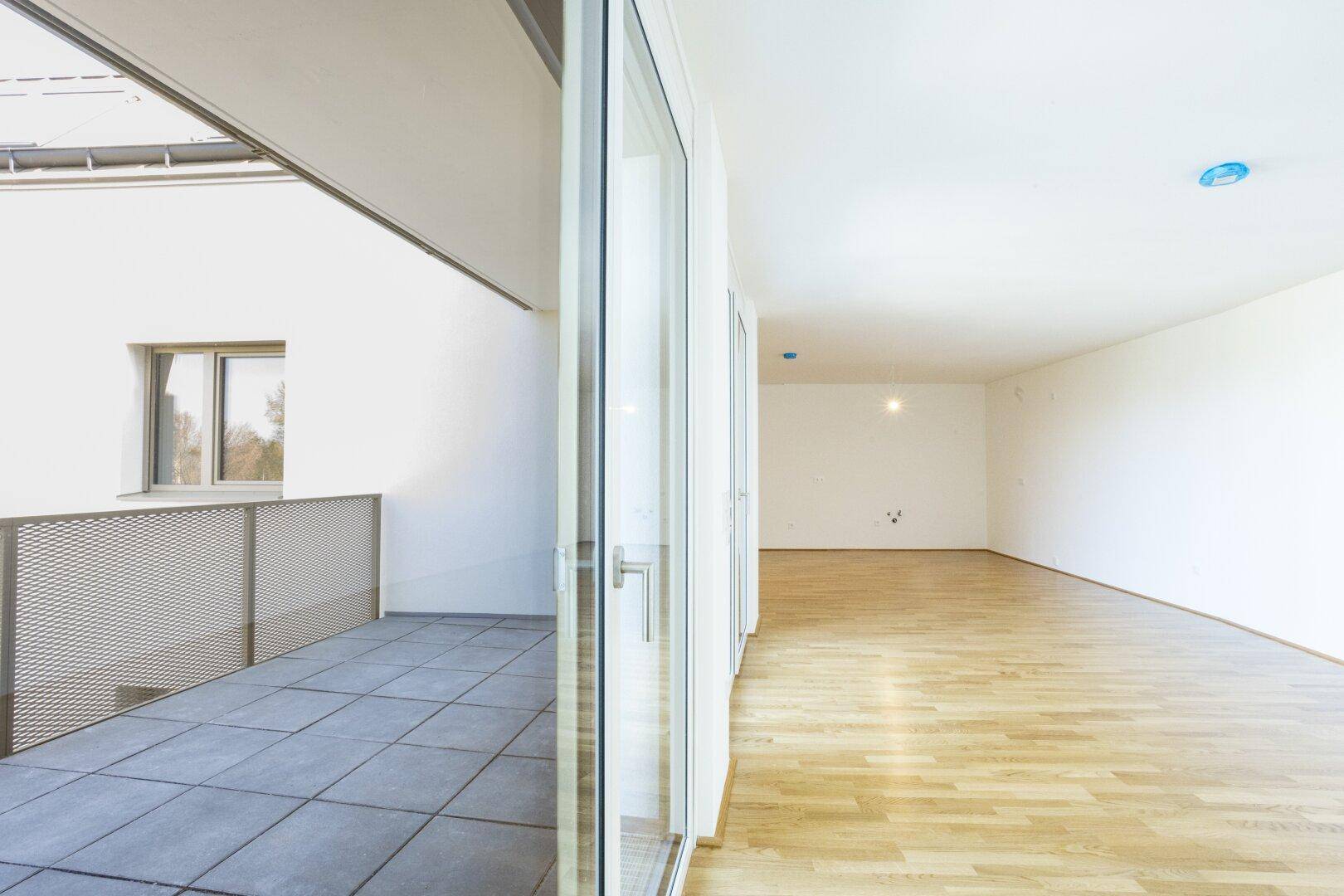 Heller Wohnbereich mit Parkettboden und Blick auf den Balkon, der zum Entspannen einlädt.