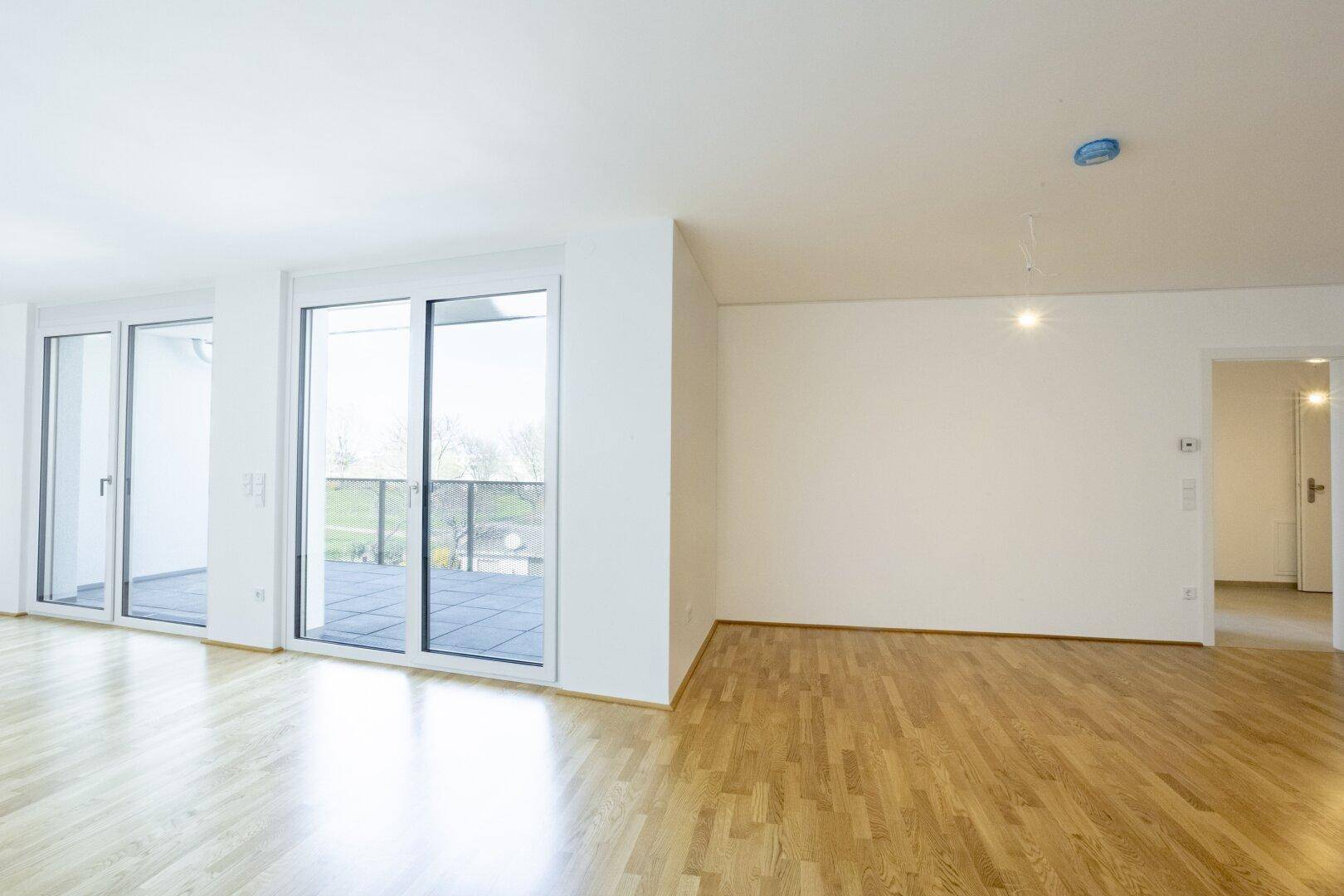 Großer Wohnbereich mit Parkettboden und Zugang zum Balkon, bietet viel Tageslicht.