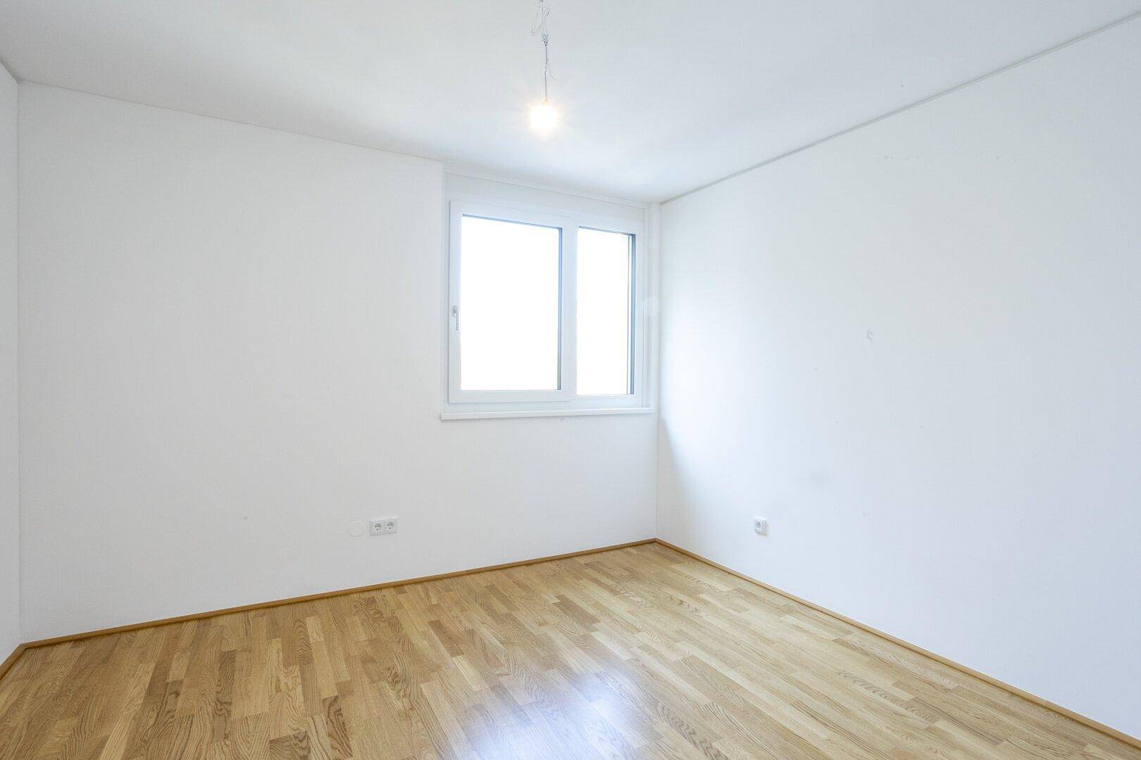 Helles Schlafzimmer mit Parkettboden und großem Fenster, bietet viel natürliches Licht.