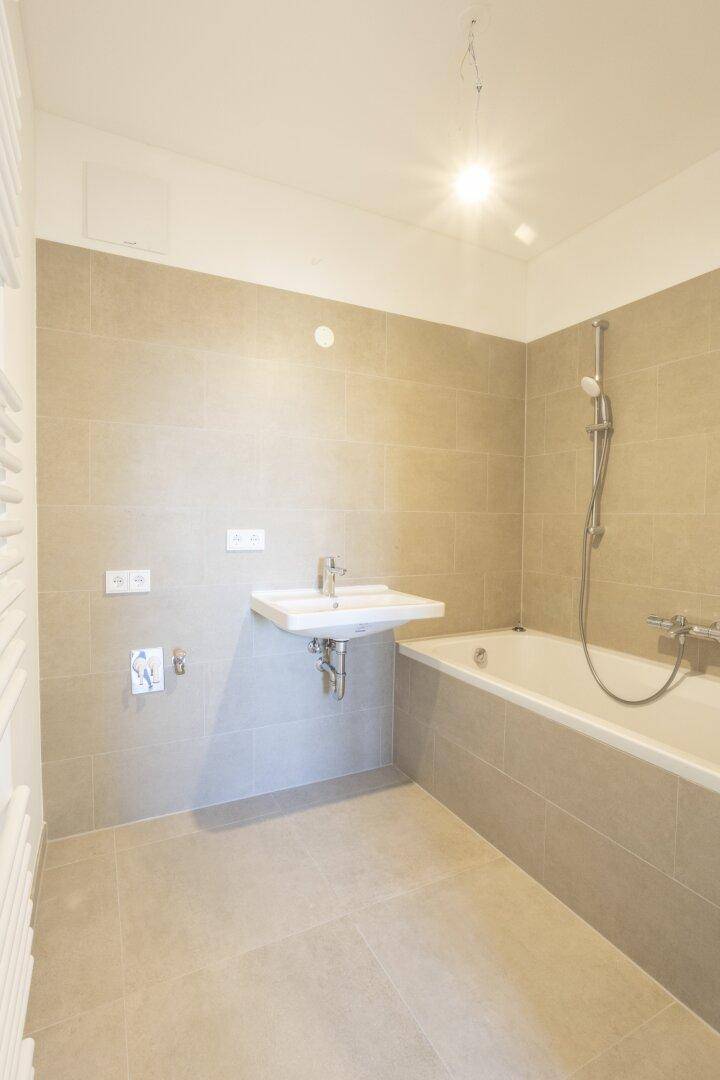 Modernes Badezimmer mit Badewanne, Waschbecken und beigefarbenen Fliesen.