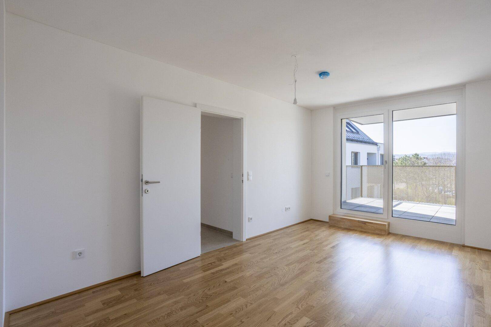 Helles Schlafzimmer mit Parkettboden und Zugang zum Balkon, bietet viel Tageslicht.