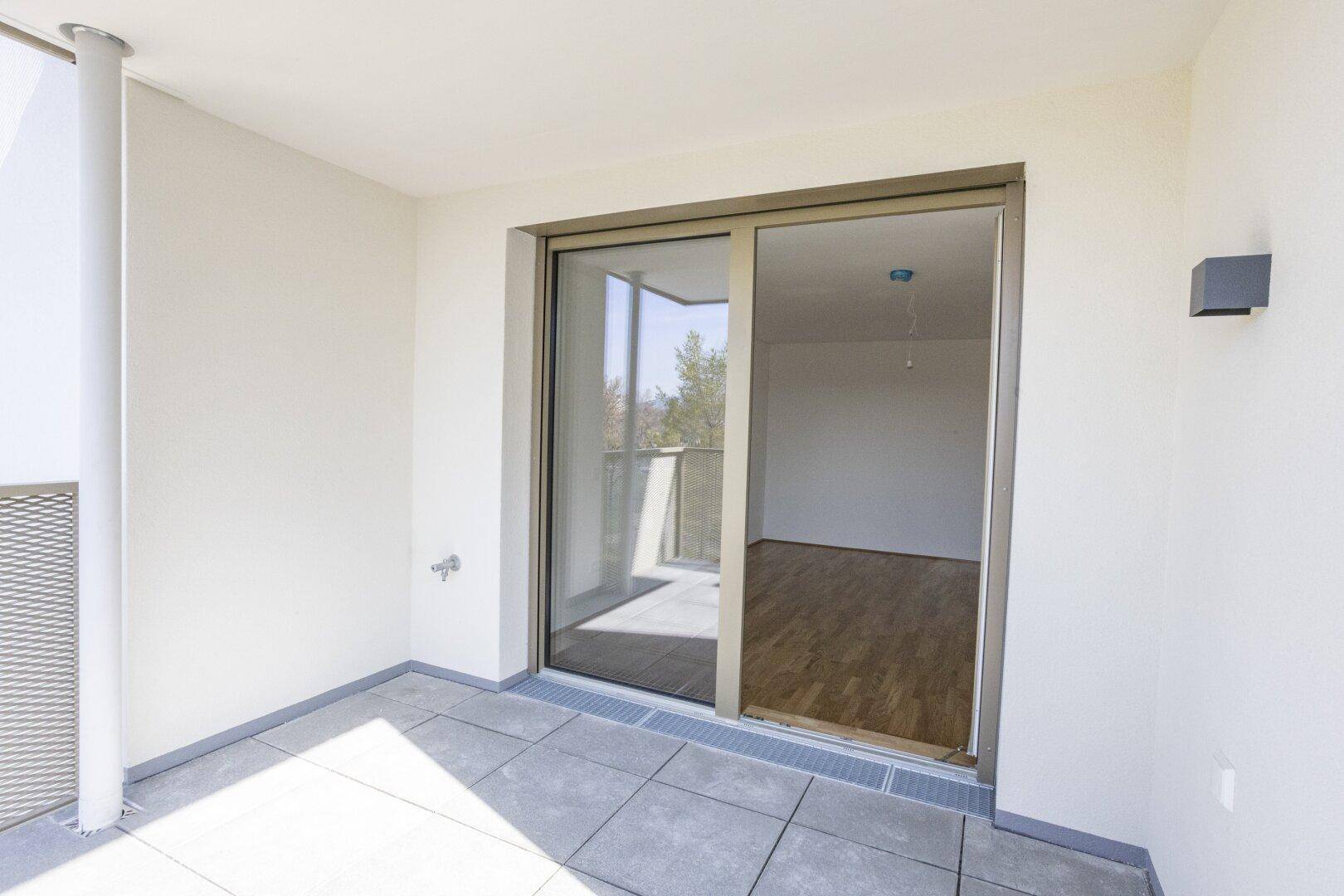 Heller Balkon mit Fliesenboden und Schiebetür zum Innenbereich, bietet viel Sonne.