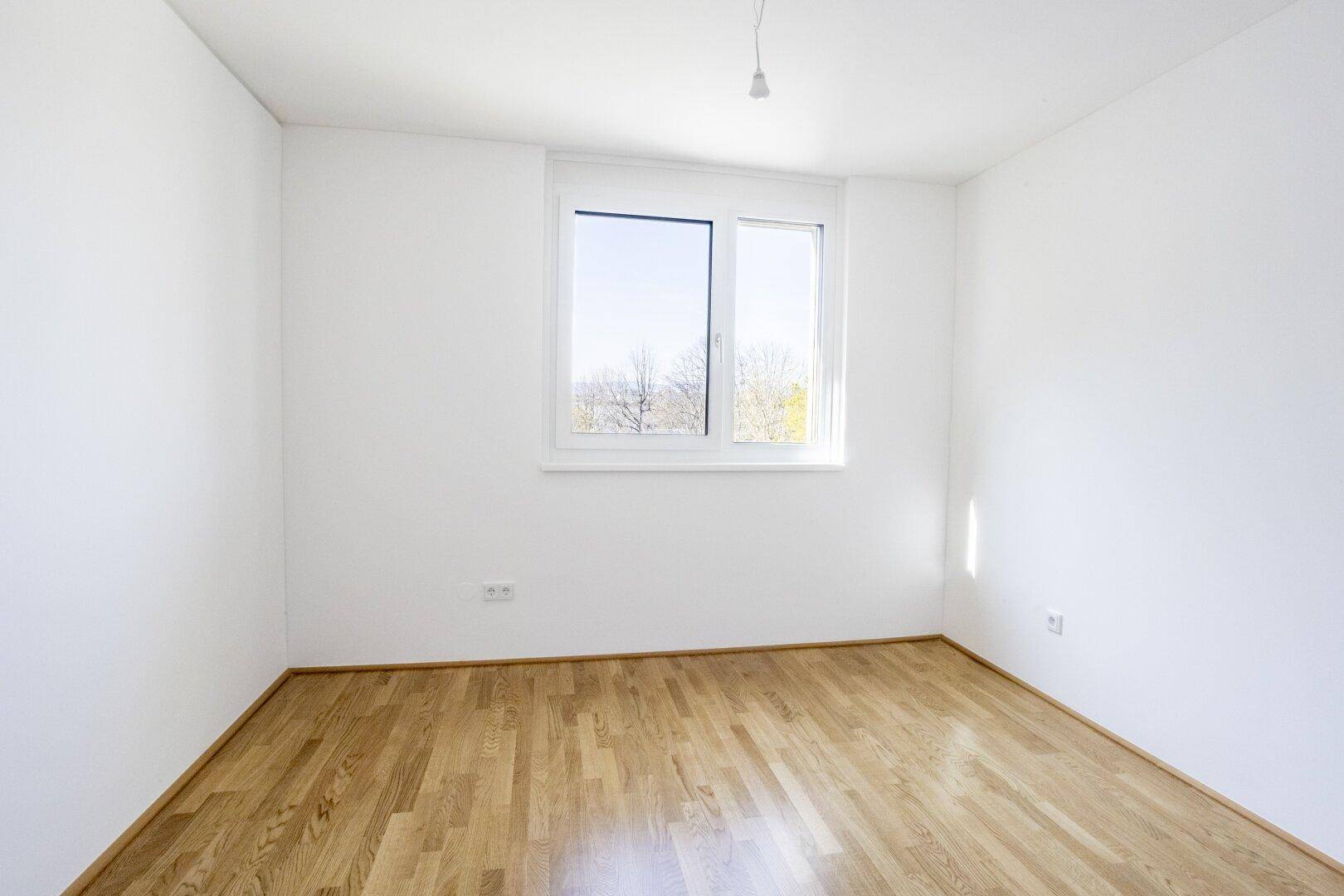 Helles Schlafzimmer mit Parkettboden und großem Fenster, bietet einen schönen Ausblick.
