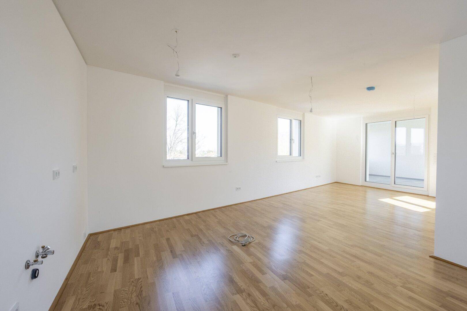 Großzügiger Wohnbereich mit hellem Parkettboden und großen Fenstern, bietet Zugang zum Balkon.