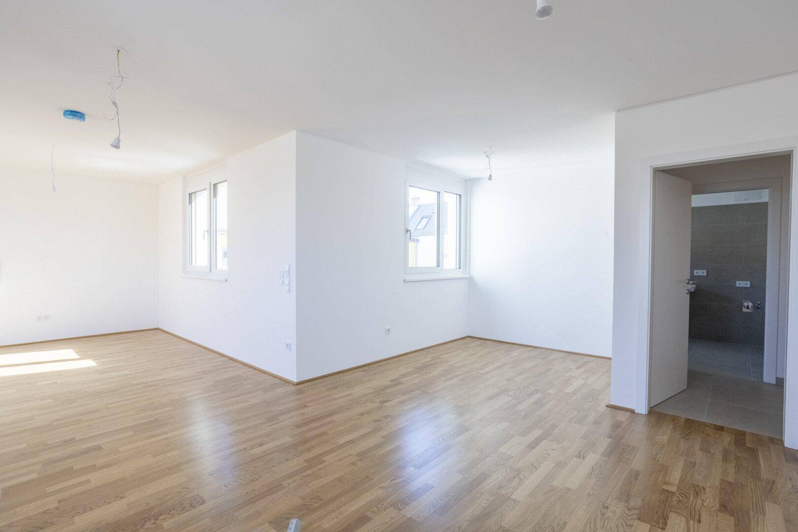 Heller Wohnraum mit Parkettboden und Fenstern, angrenzend an ein modern gefliestes Badezimmer.