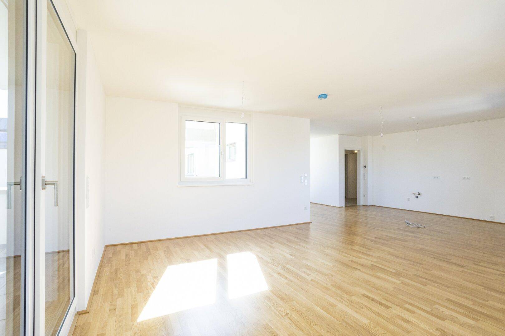 Lichtdurchfluteter Wohnbereich mit Parkettboden und großer Balkontür, bietet viel Tageslicht.