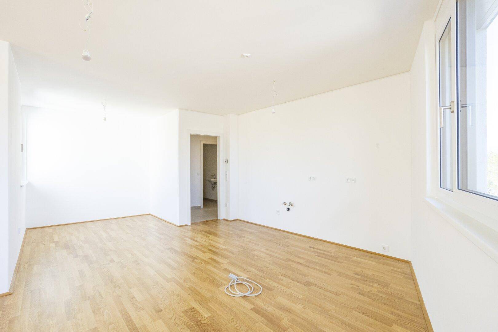 Geräumiger Wohnbereich mit Parkettboden und Fenster, mit Blick auf den Eingang zum Badezimmer.