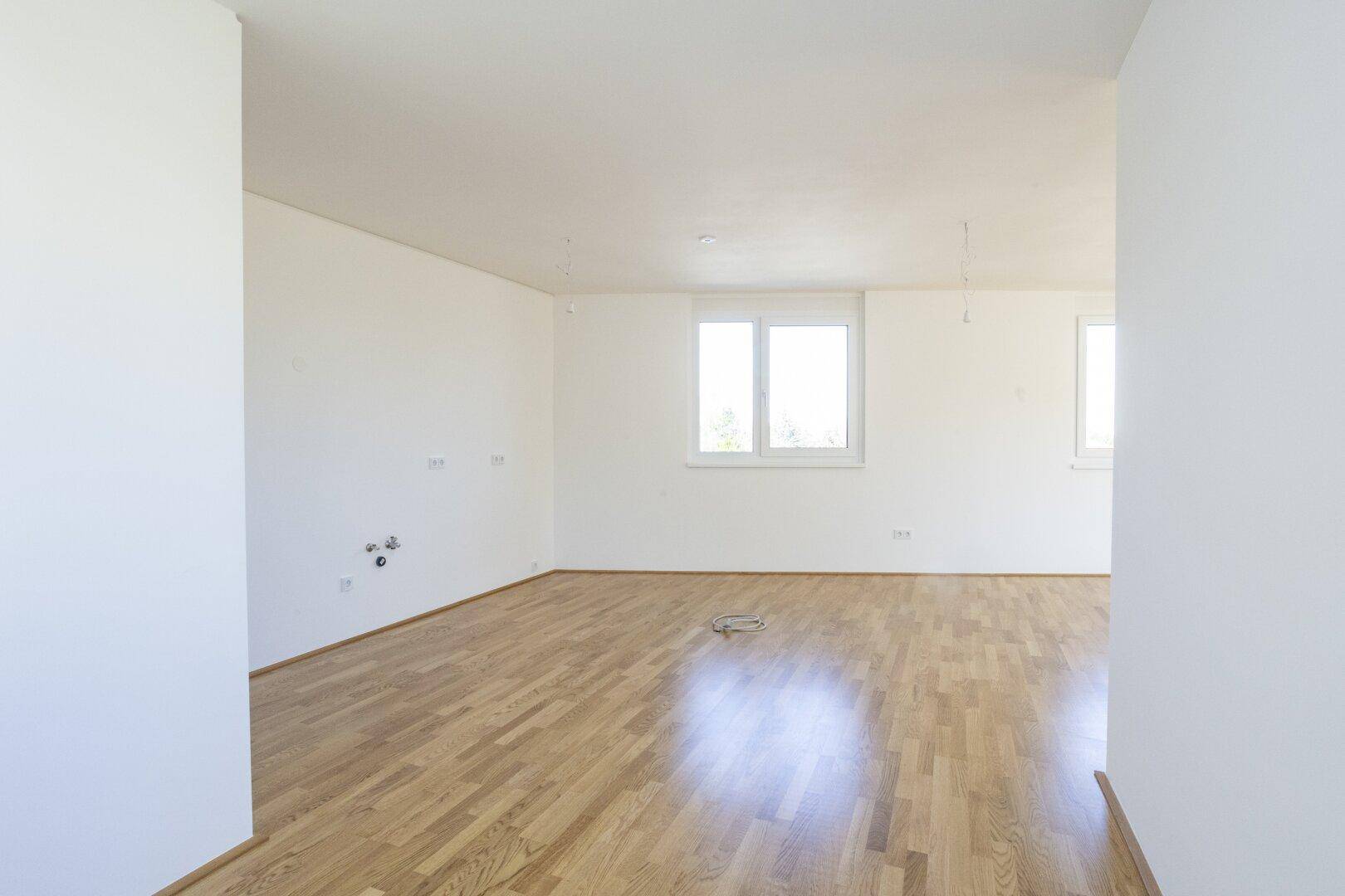 Heller und leerer Wohnraum mit Parkettboden und mehreren Fenstern, bereit zur individuellen Gestaltung.