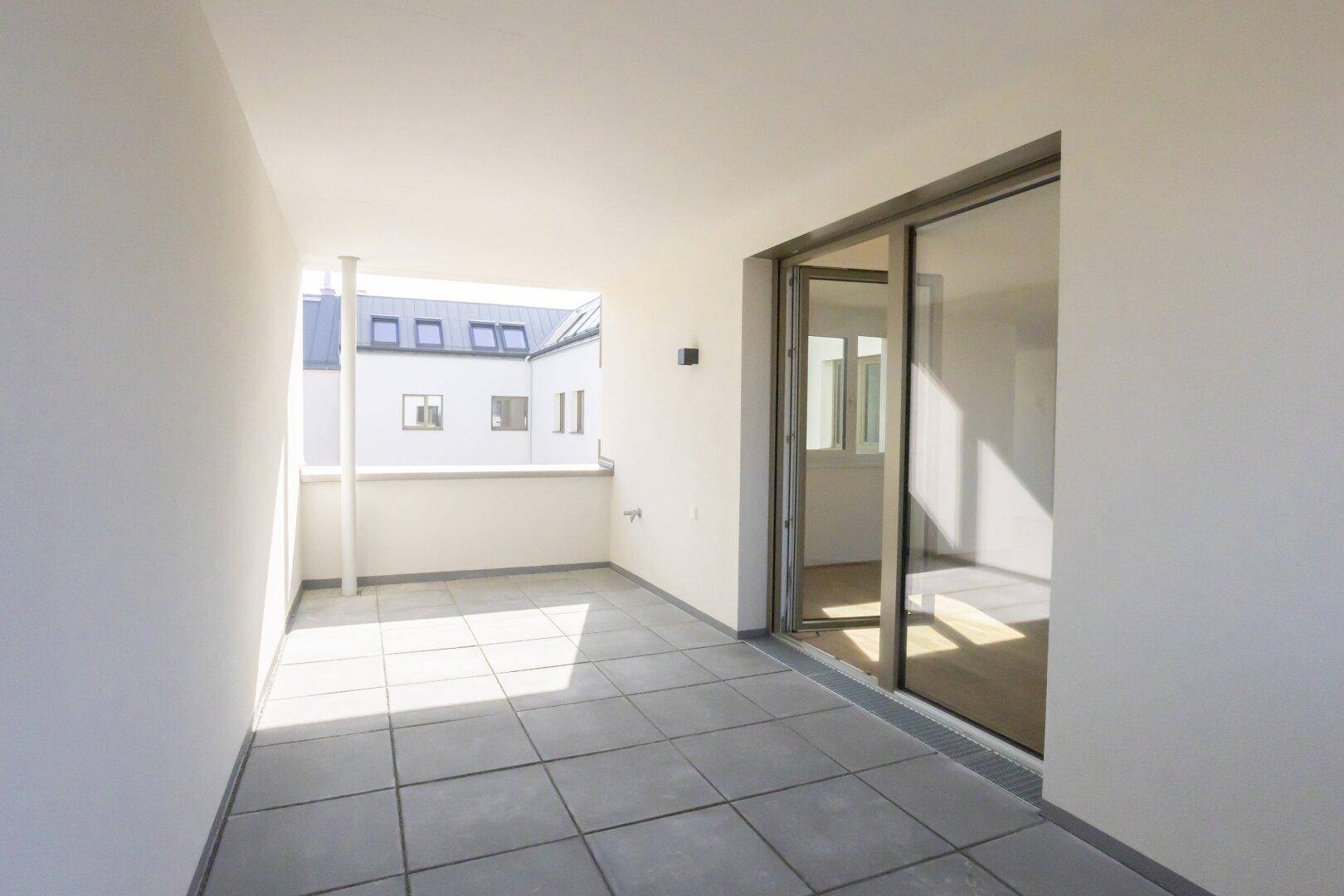 Sonniger Balkon mit grauen Fliesen und Blick auf den Innenhof, ideal zum Entspannen im Freien.