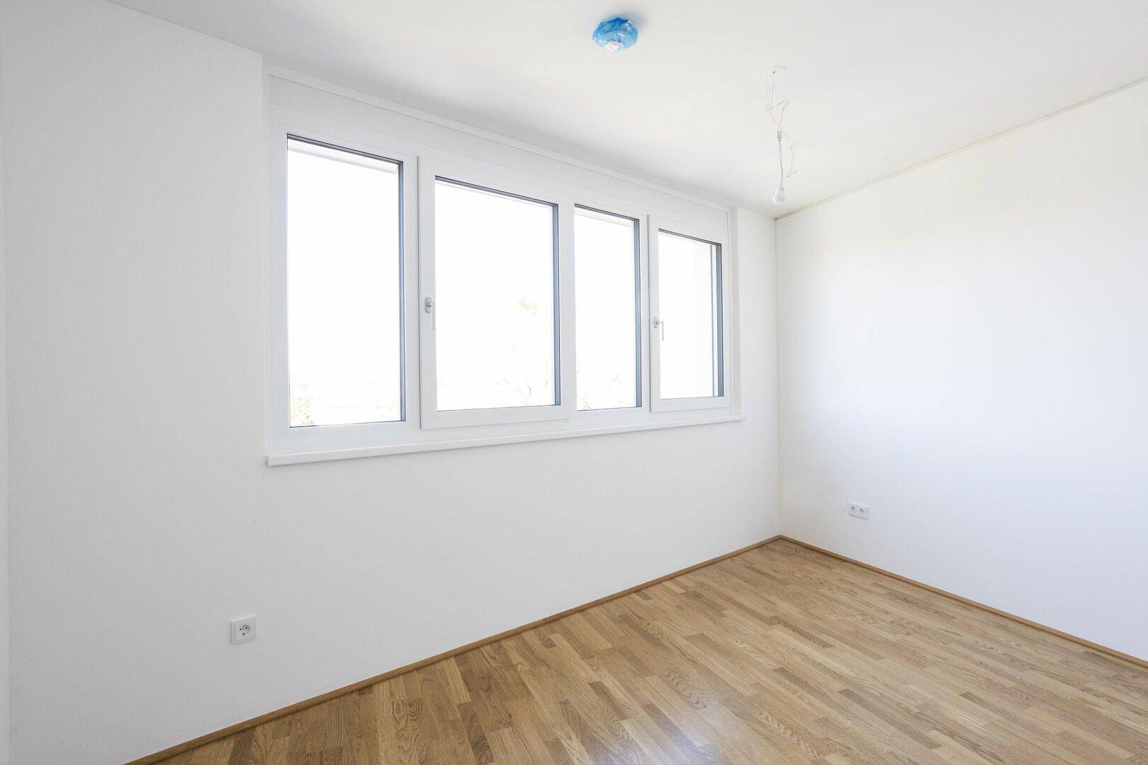 Helles Schlafzimmer mit Parkettboden und großer Fensterfront, bietet viel Tageslicht und Ausblick.