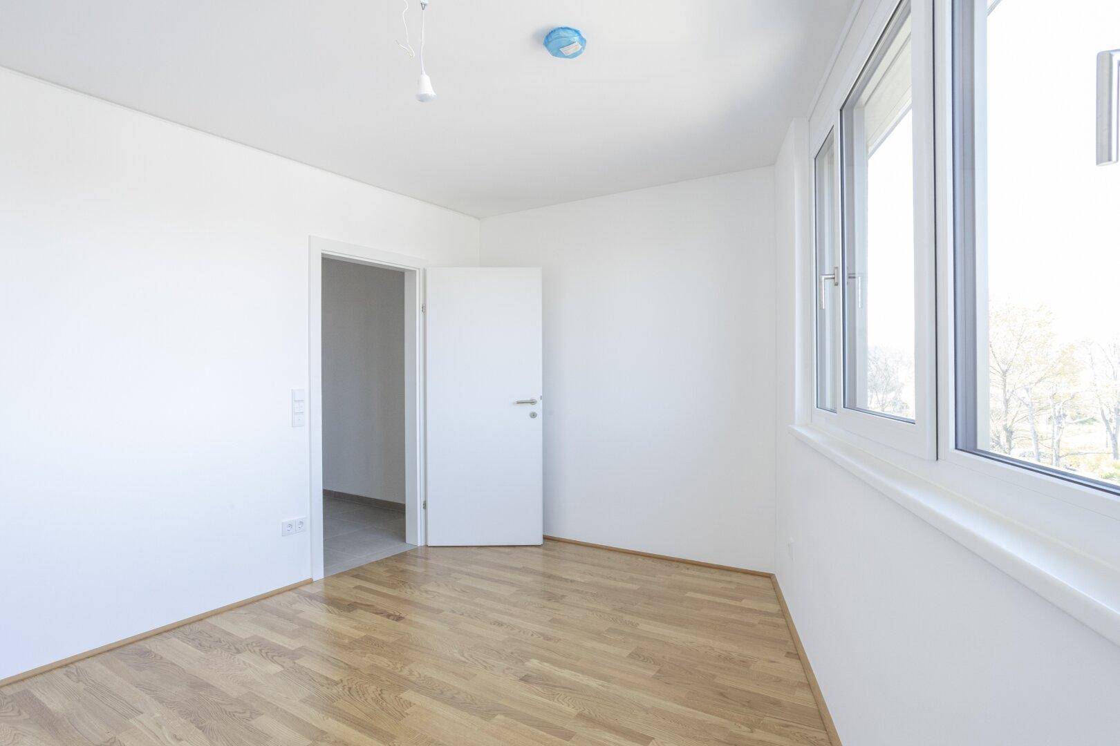 Geräumiges Schlafzimmer mit Parkettboden und Fenster, mit Zugang zu einem weiteren Raum.