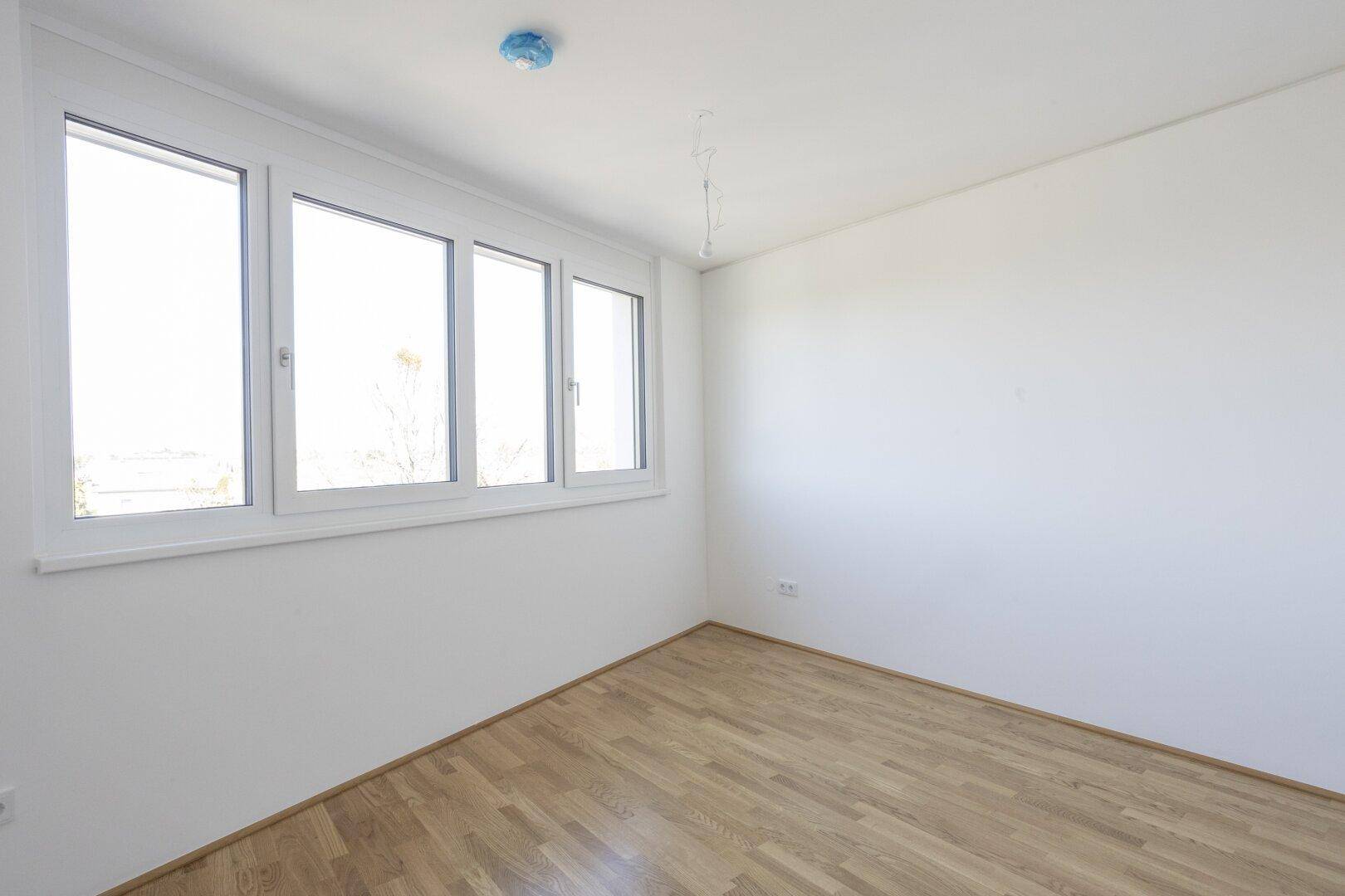 Lichtdurchflutetes Schlafzimmer mit Parkettboden und breiter Fensterfront, ideal für erholsame Nächte.