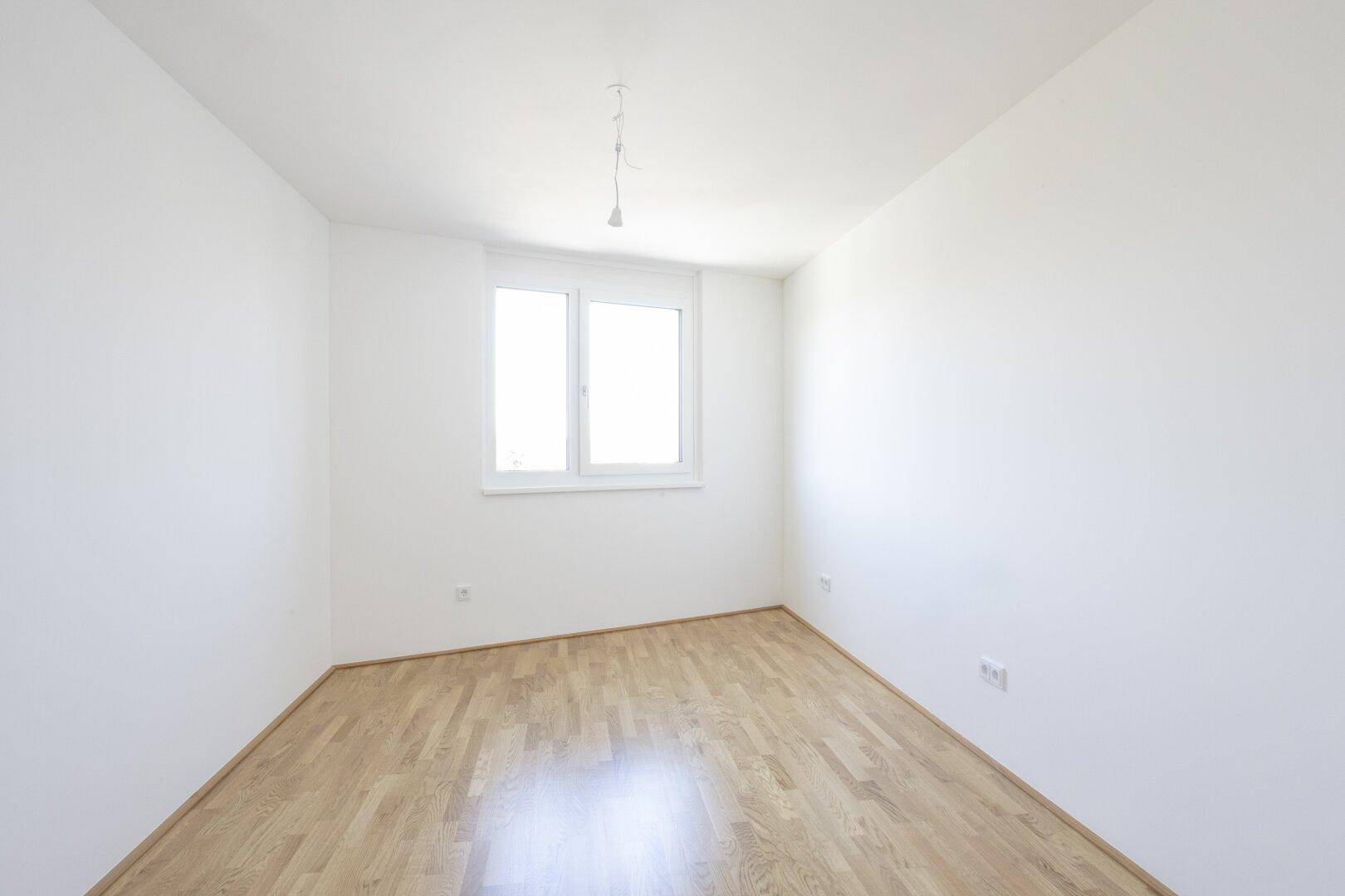 Helles Schlafzimmer mit Parkettboden und einem Fenster, bietet eine ruhige und angenehme Atmosphäre.