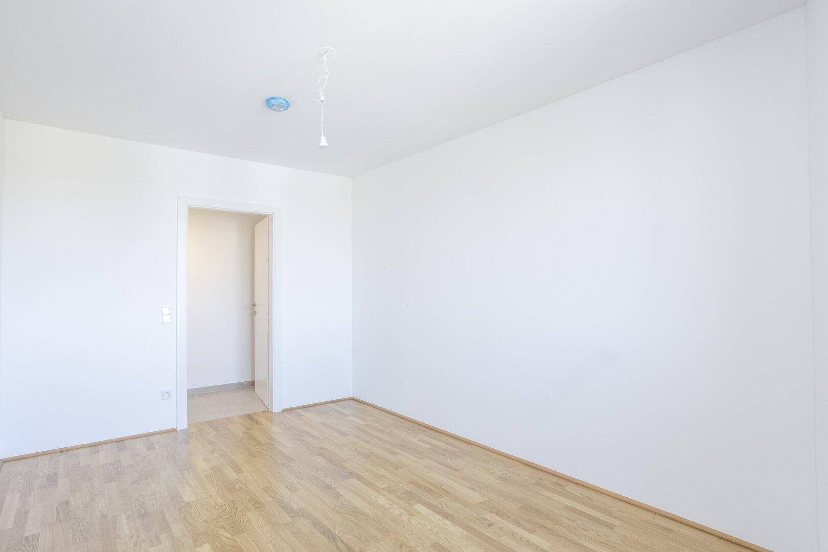 Geräumiges Schlafzimmer mit Parkettboden und offener Tür, bereit zur individuellen Einrichtung.
