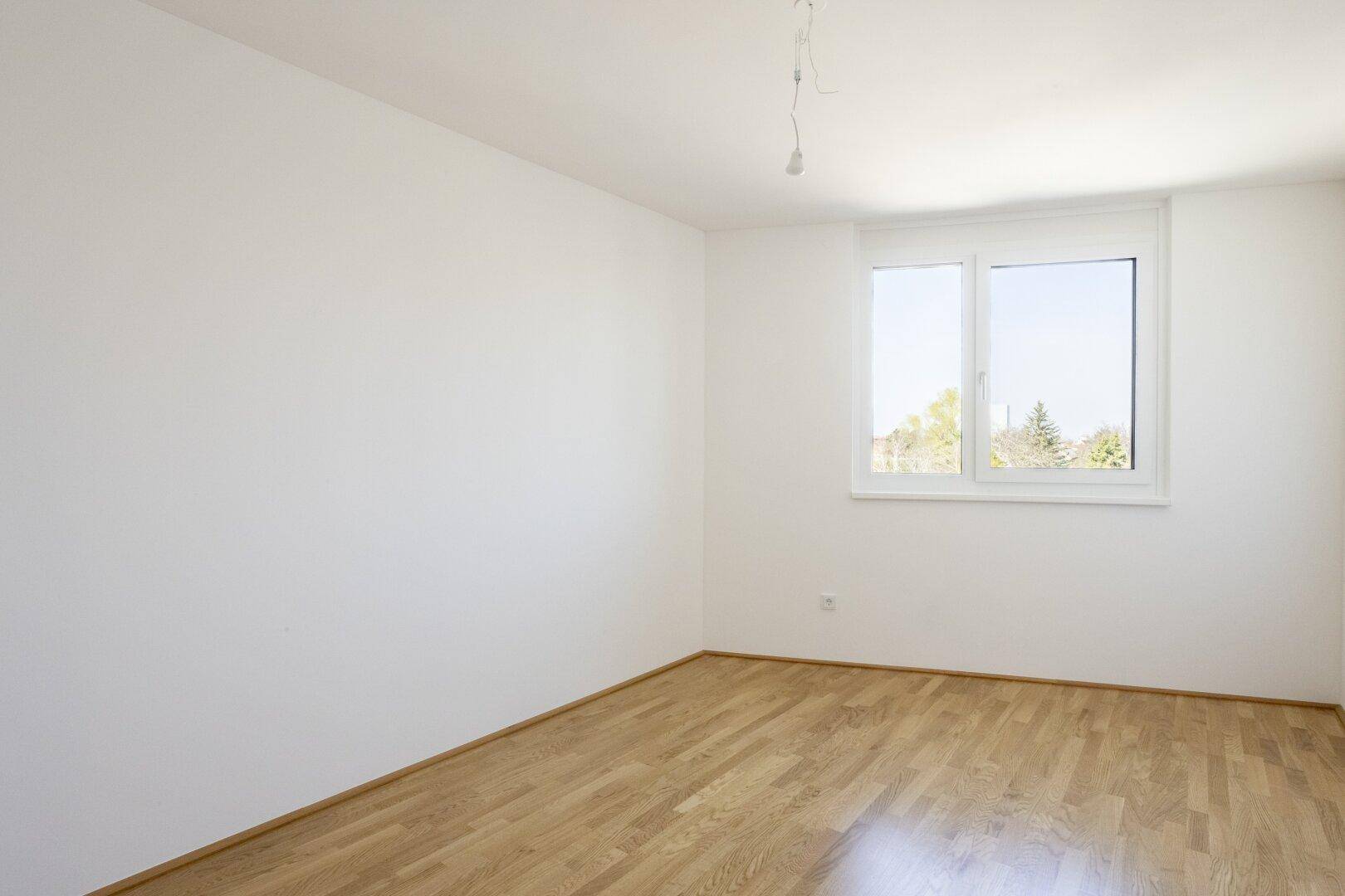 Helles Schlafzimmer mit Parkettboden und Fenster, bietet einen angenehmen Ausblick und viel Licht.