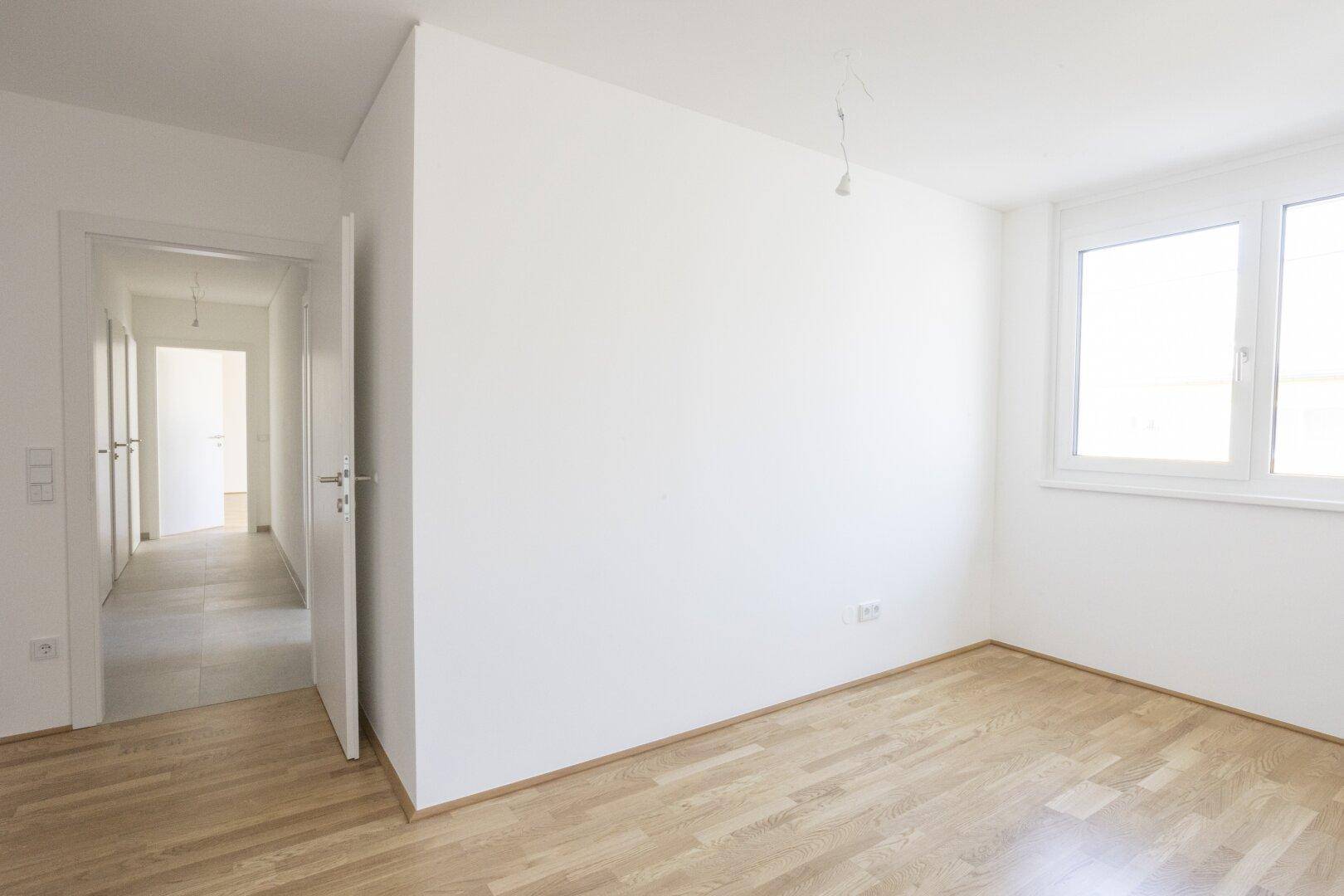 Leerer Raum mit Holzboden und einem großen Fenster, bereit zur individuellen Gestaltung.