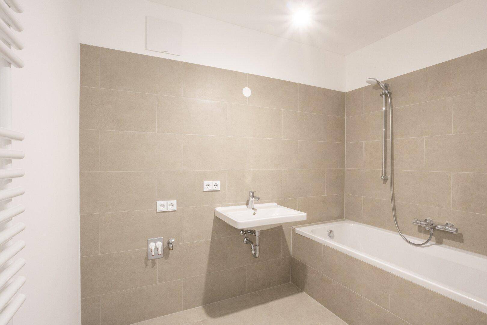 Modernes Badezimmer mit Badewanne, Waschbecken und beheiztem Handtuchhalter an der Wand.