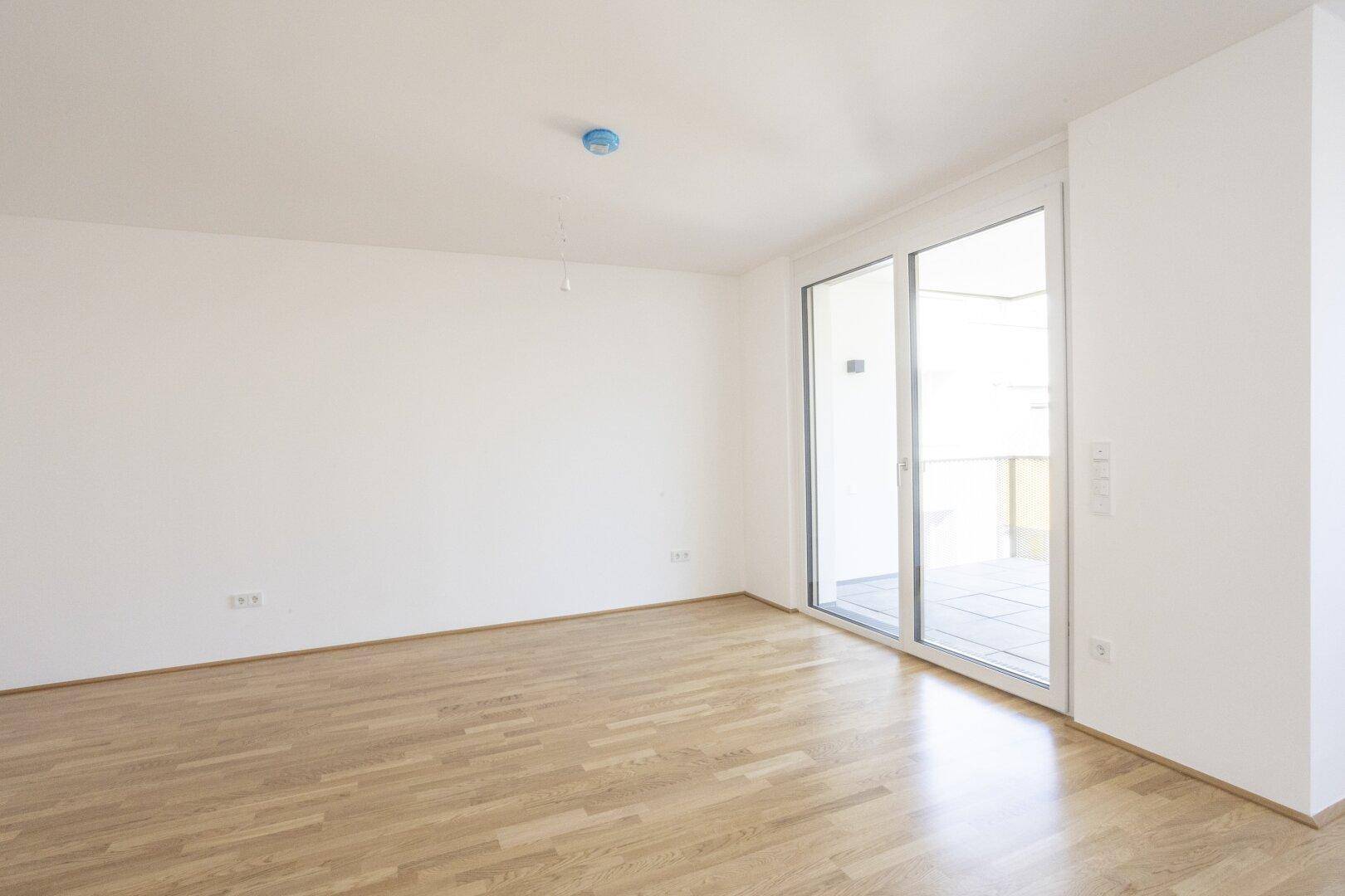 Geräumiges Wohnzimmer mit Holzboden und Zugang zu einem sonnigen Balkon.