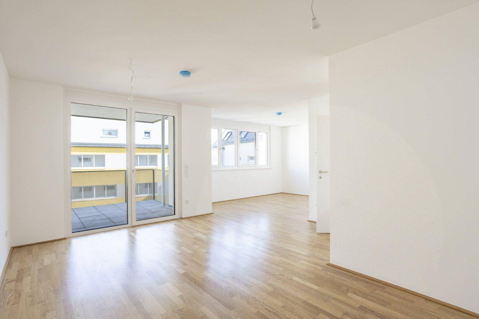 Heller Wohnbereich mit Holzboden, Balkonzugang und mehreren Fenstern für viel Licht.