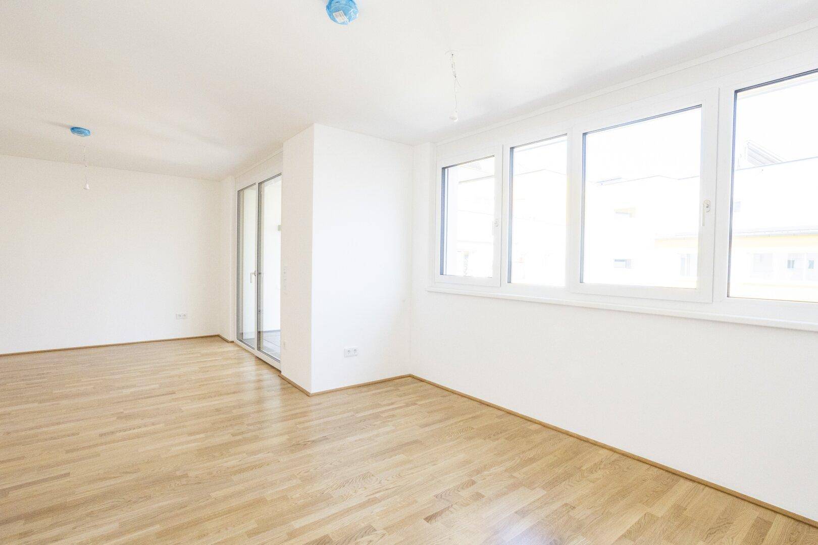 Geräumiger Raum mit Holzboden, großen Fenstern und Zugang zum Balkon.