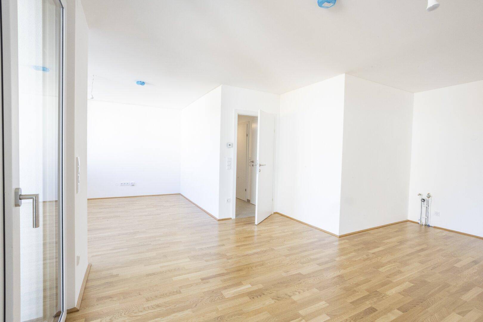 Leerer Küchenbereich mit Holzboden, Türzugang und Anschlüssen für eine Einbauküche.