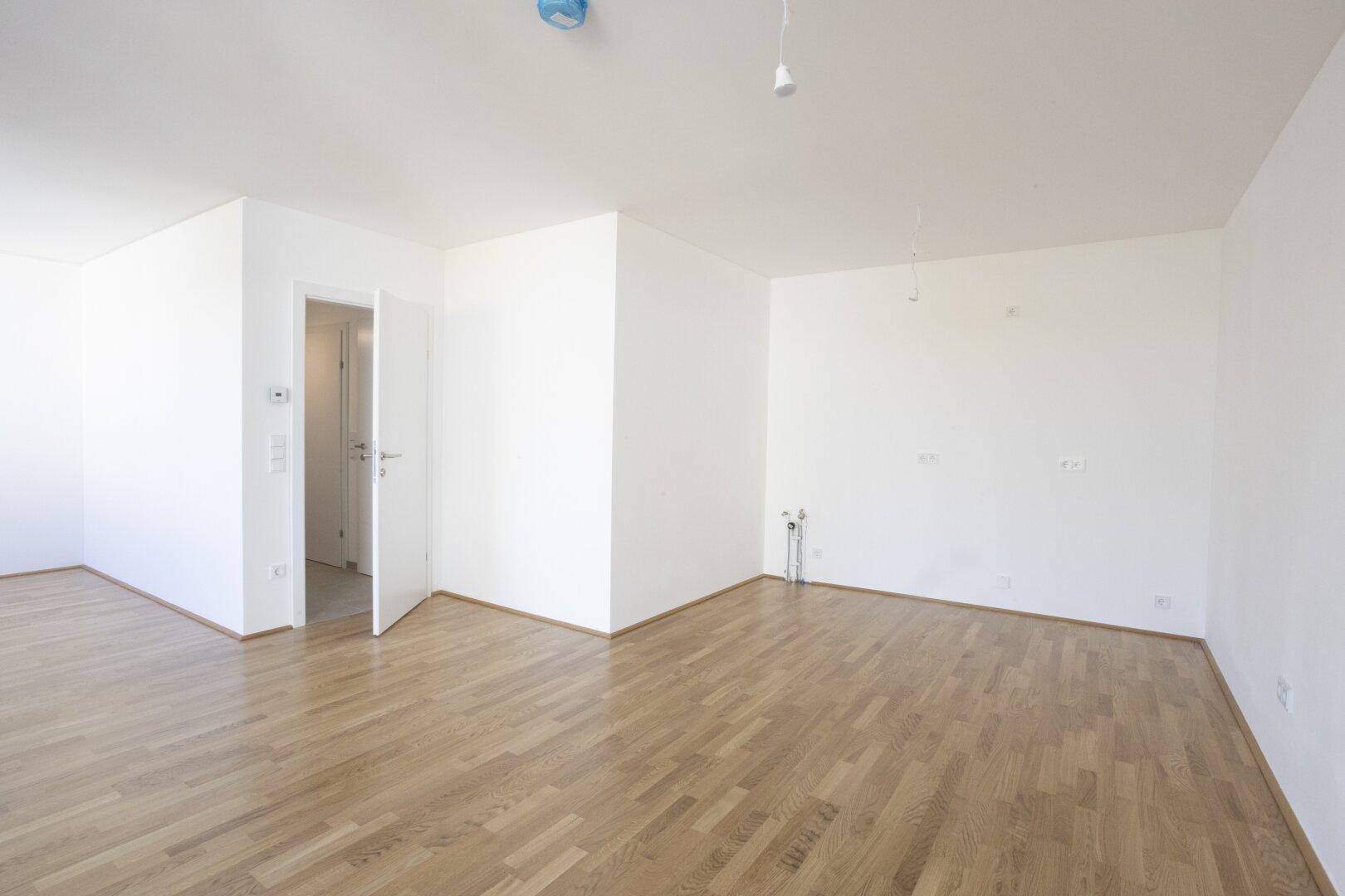 Großer Raum mit Holzboden und Anschlüssen für eine zukünftige Küche, bereit zur Gestaltung.
