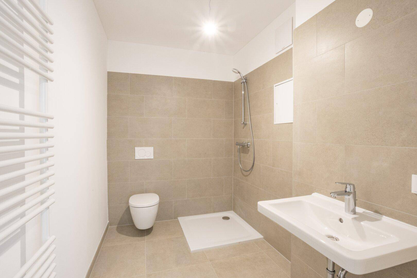 Modernes Badezimmer mit Dusche, WC, Waschbecken und beigefarbenen Fliesen.