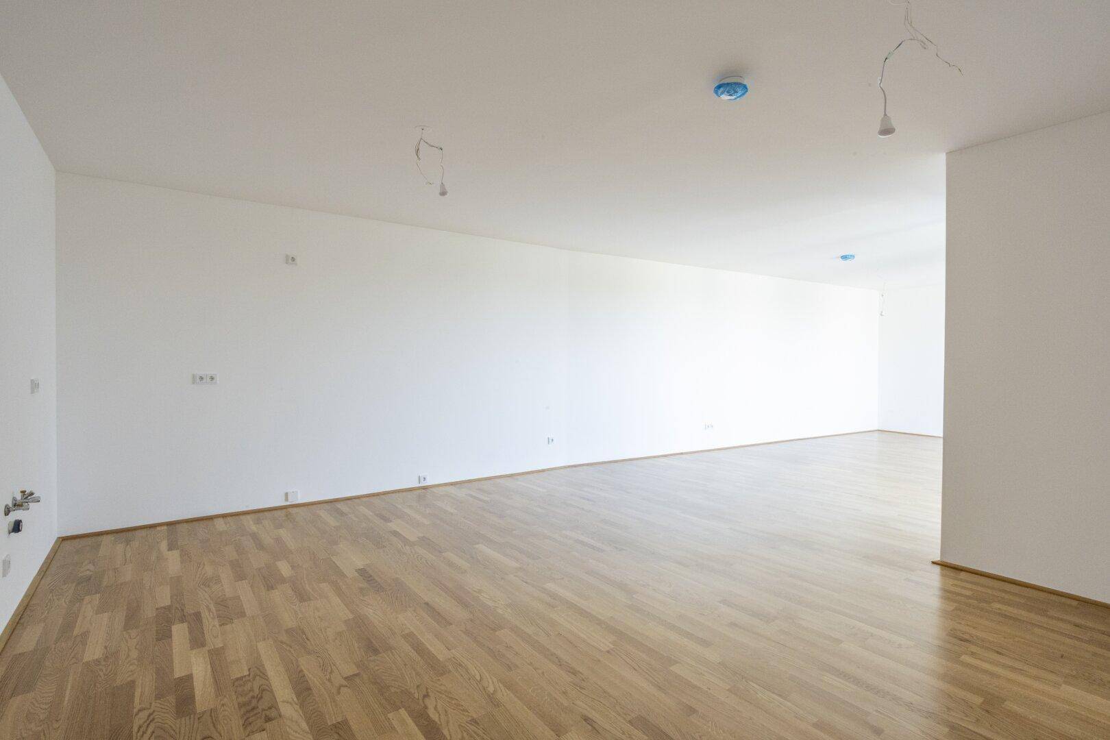 Geräumiges, helles Zimmer mit Holzboden und weißen Wänden, bereit zur Einrichtung.