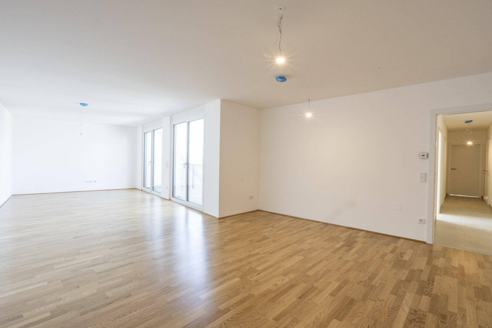 Heller Wohnbereich mit Holzboden und großen Fenstern, die viel Tageslicht hereinlassen.