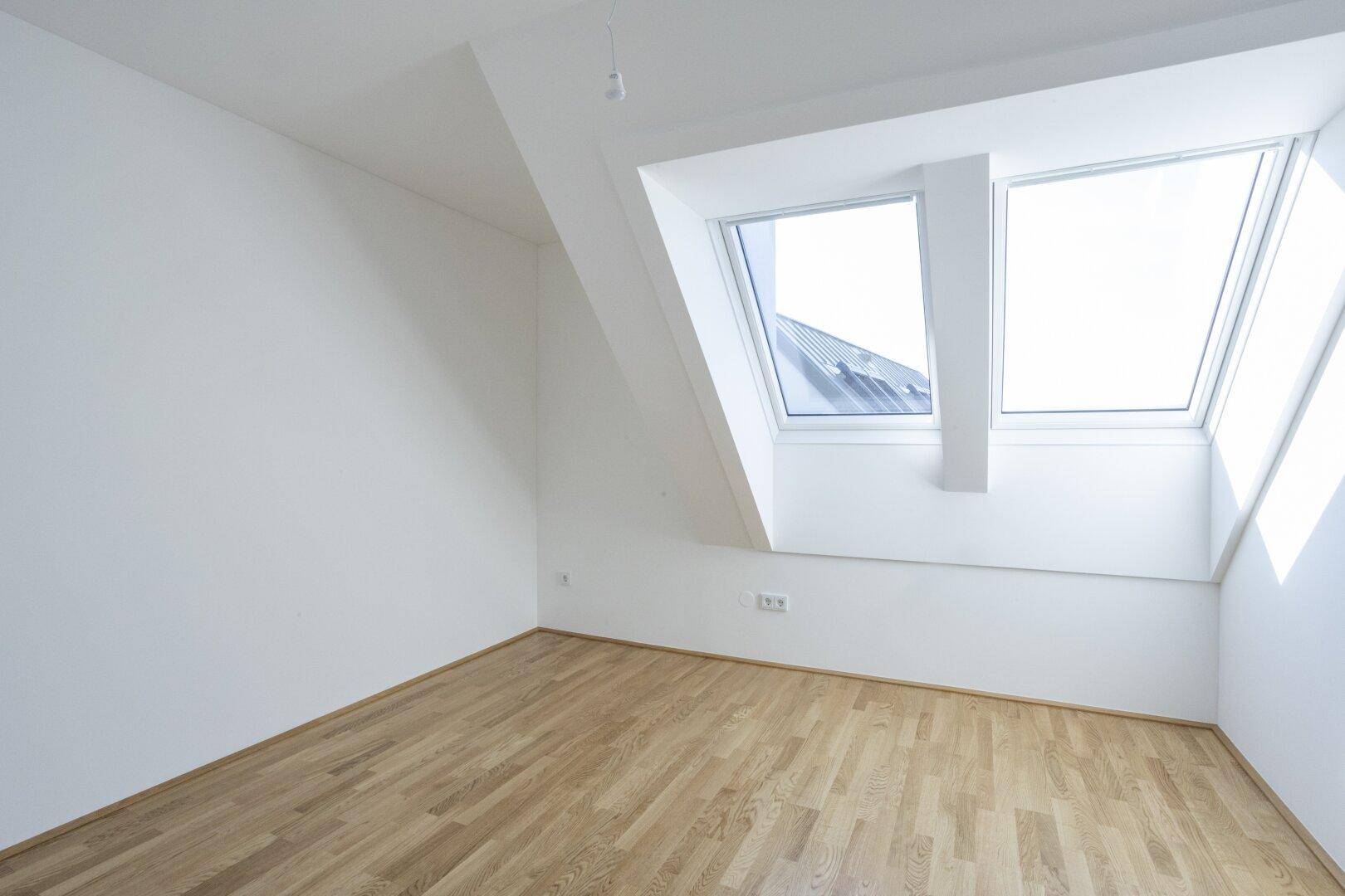 Helles Dachzimmer mit Holzboden, schrägen Wänden und Dachfenstern für viel Licht.