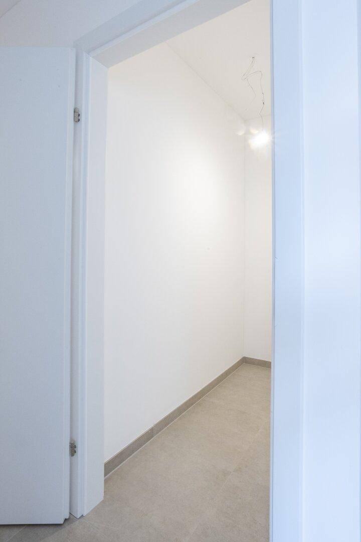 Schmaler, heller Flur mit Fliesenboden und weißen Wänden, der zu einem weiteren Bereich führt.