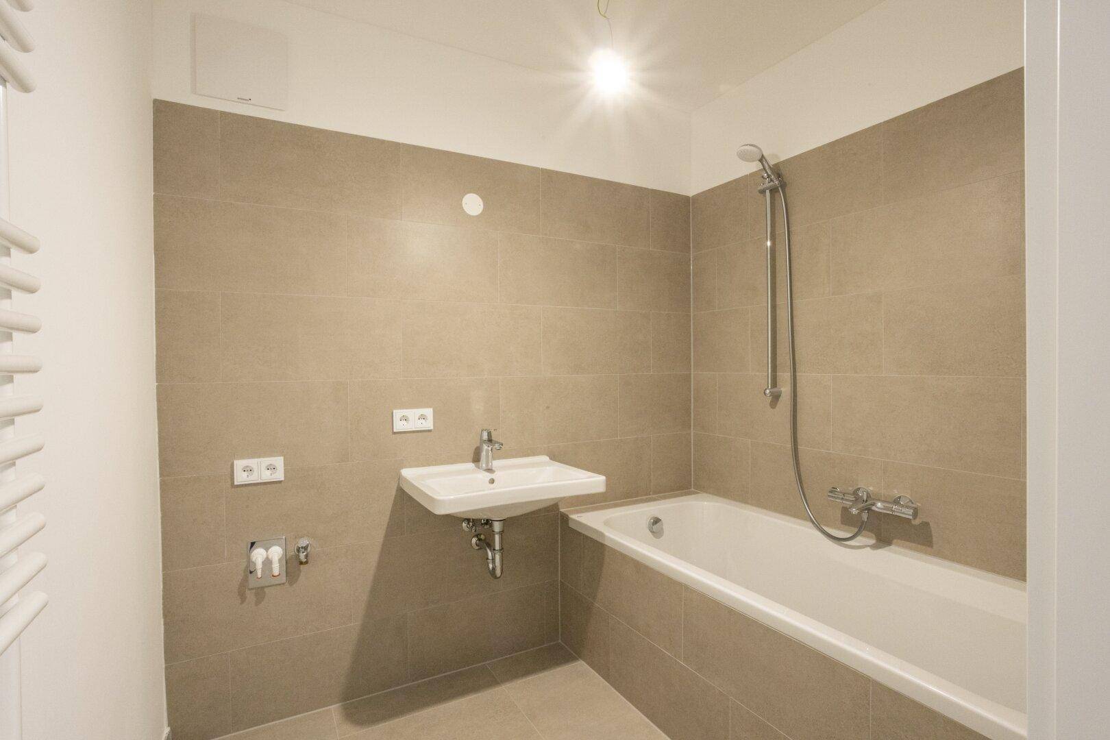 Modernes Badezimmer mit Badewanne, Waschbecken und beigefarbenen Wand- und Bodenfliesen.