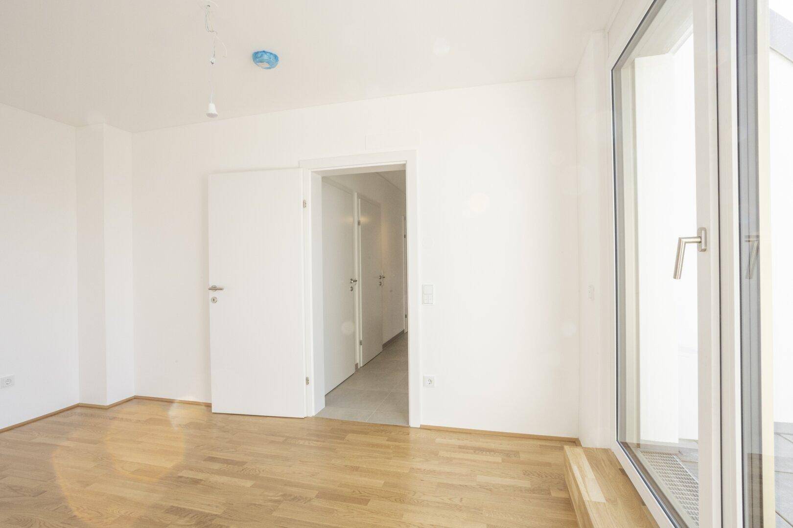 Helles Zimmer mit Holzboden und Zugang zu einem Flur, ideal als Schlaf- oder Arbeitszimmer.