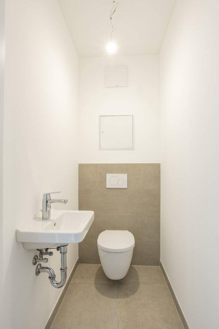 Kleines, modernes Gäste-WC mit Wand-WC und Handwaschbecken in neutralen Farben.