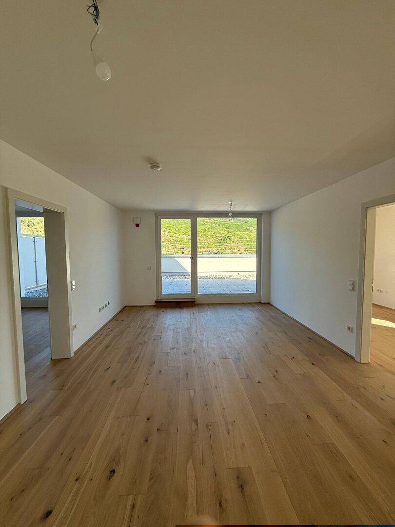 Heller, leerer Raum mit Holzboden und großer Glasfront zum Außenbereich.