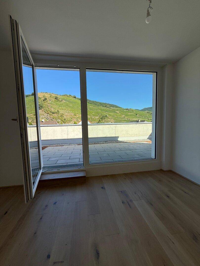 Lichtdurchfluteter Raum mit großen Fenstern, Holzboden und beeindruckendem Weinbergblick.