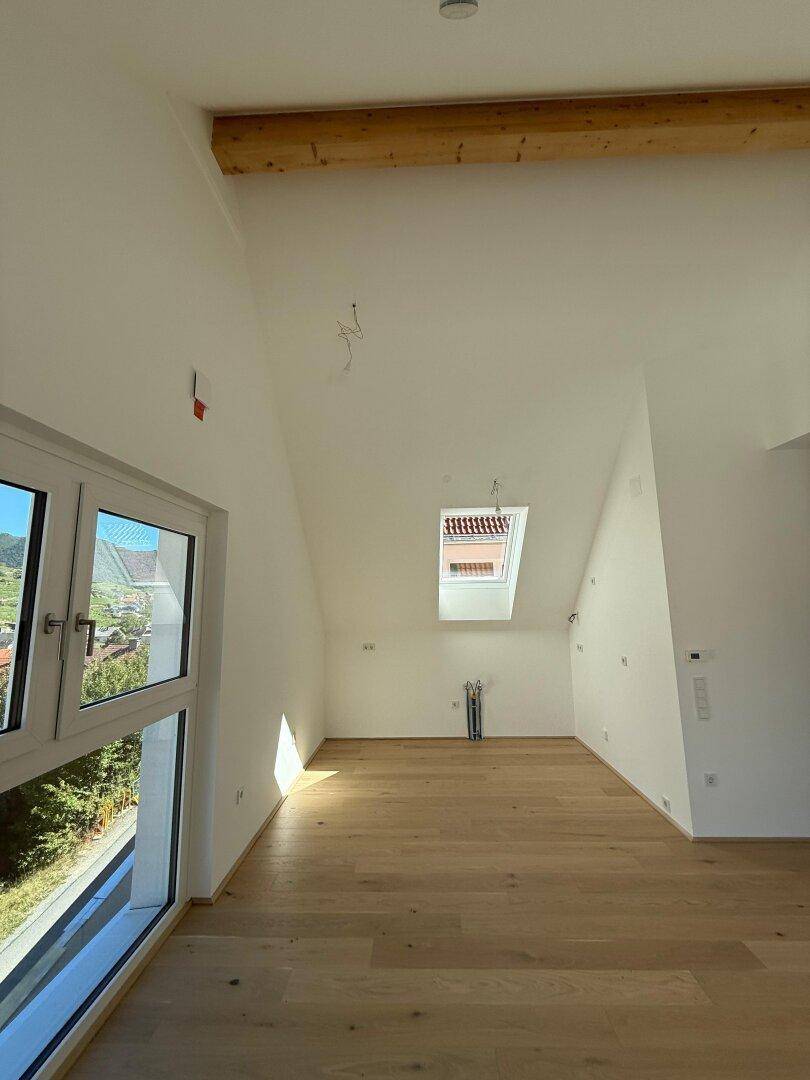 Heller Raum im Dachgeschoss mit Holzbalken, Dachfenster und hochwertigem Parkettboden.