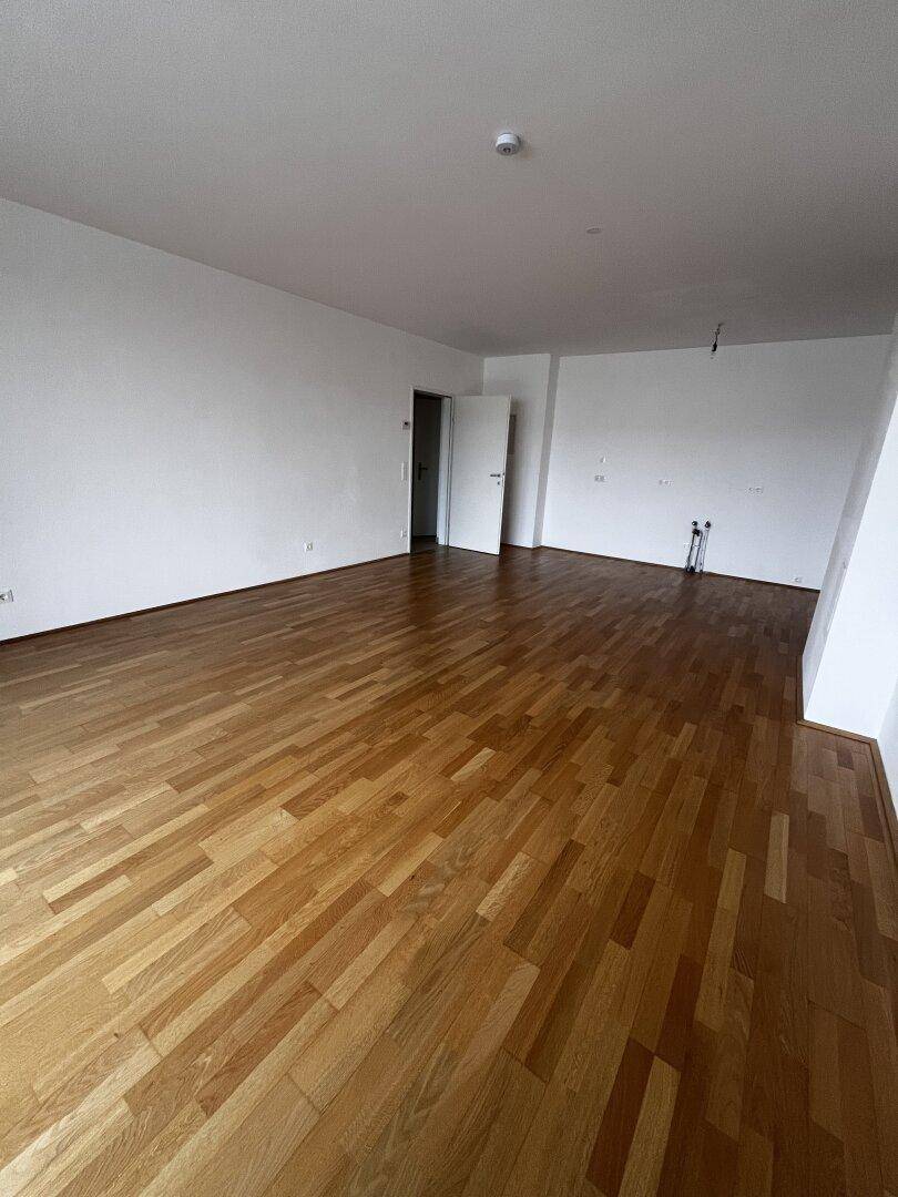 Heller, leerer Raum mit Parkettboden und Anschlüssen für eine zukünftige Küche.