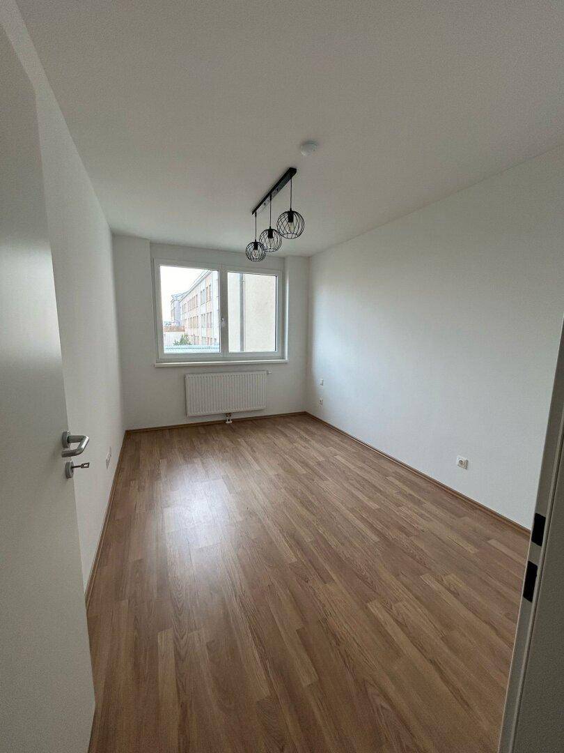 Heller, leerer Raum mit Holzfußboden und großem Fenster, ideal als Schlaf- oder Arbeitszimmer.