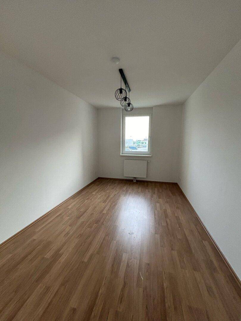 Lichtdurchfluteter Raum mit Parkettboden und modernem Deckenlicht, bereit zur individuellen Gestaltung.