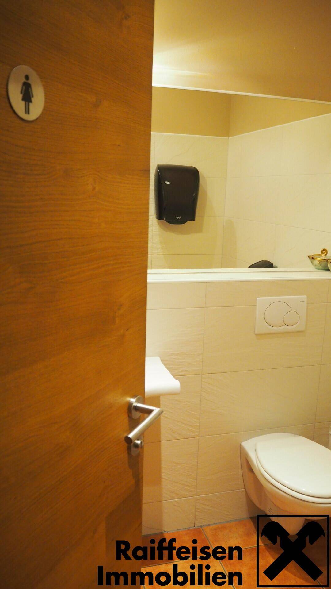 Saubere Toilette mit Wand-WC, Handtrockner und Fliesen an den Wänden, gut gepflegt und funktional.